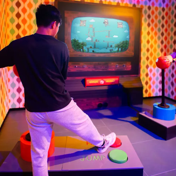 Ein Spieler tritt auf das Sprungpad vor dem Arcade-Bildschirm von Hangry Monkey