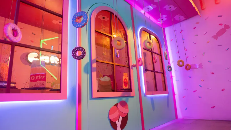 Dentro de la sala Candit — una tienda de golosinas de neón con donuts colgados como dianas