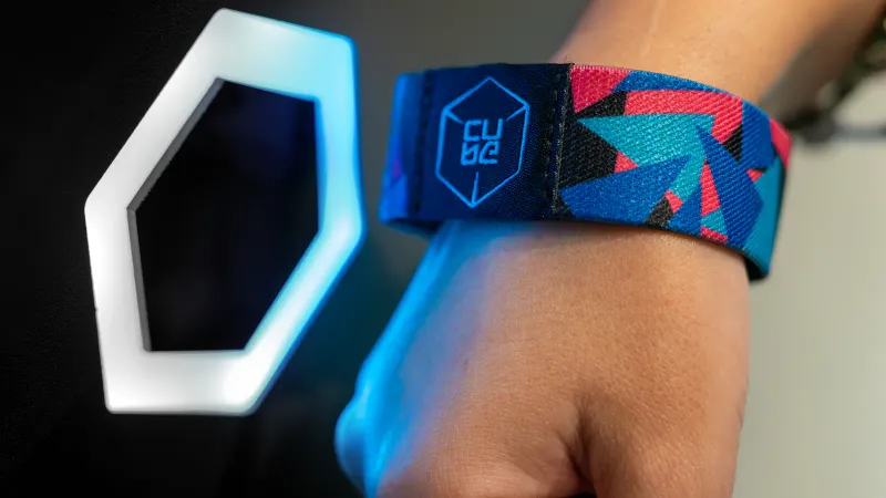 Una pulsera RFID CUBE acercada a un lector hexagonal iluminado en la puerta de una sala